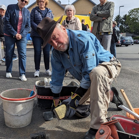 Der Künstler Gunter Demnig lässt den Stolperstein in den Asphalt ein. Neben ihn ein Eimer mit Zement.