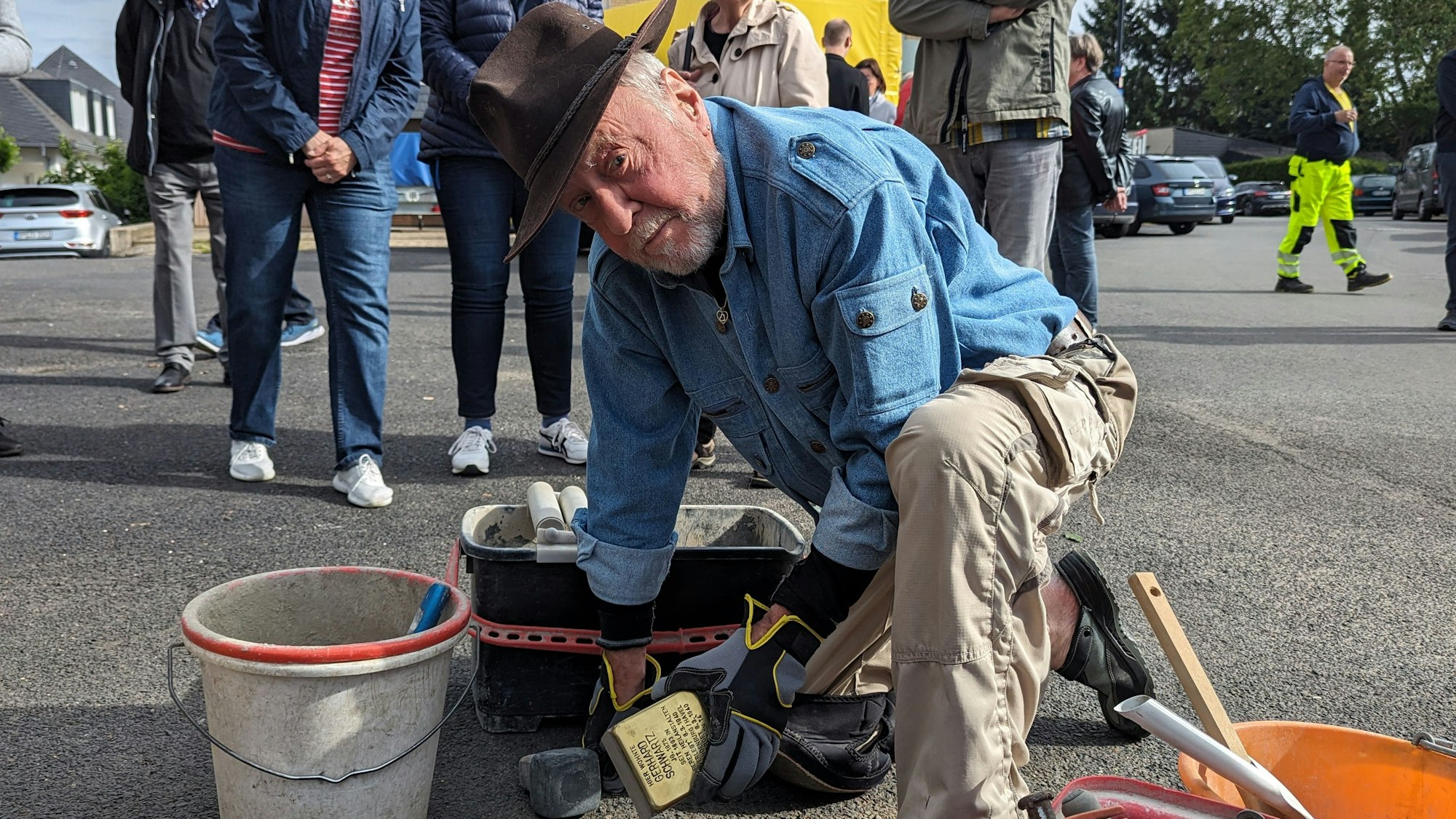 Der Künstler Gunter Demnig lässt den Stolperstein in den Asphalt ein. Neben ihn ein Eimer mit Zement.