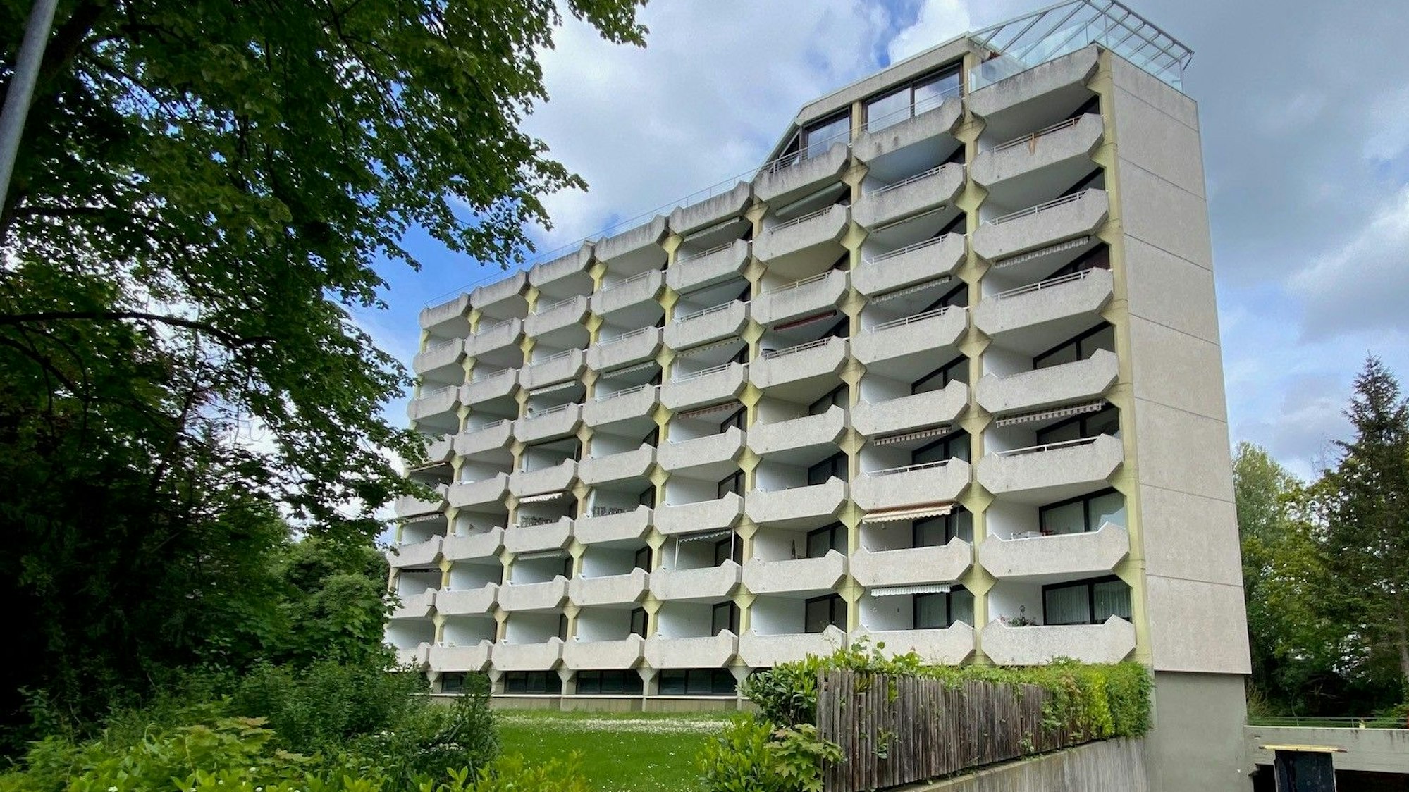 Zu sehen ist ein Mehrfamilienhaus hinter Bäumen.