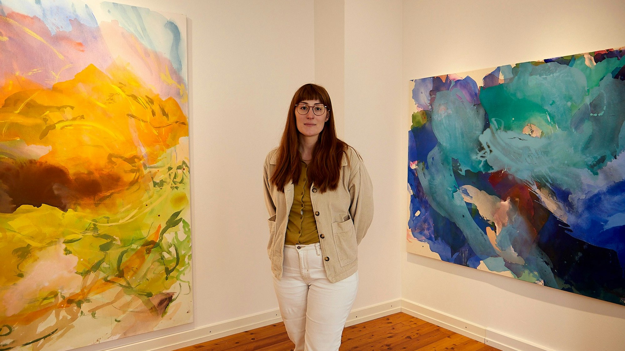 Sophia Büthe steht zwischen zwei Bildern in intensiven Farben.
