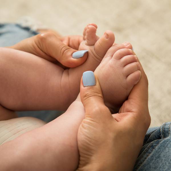 Eine Frau mit hellblau lackierten Fingernägeln hält die kleinen Füße eines Babys in ihren Händen.