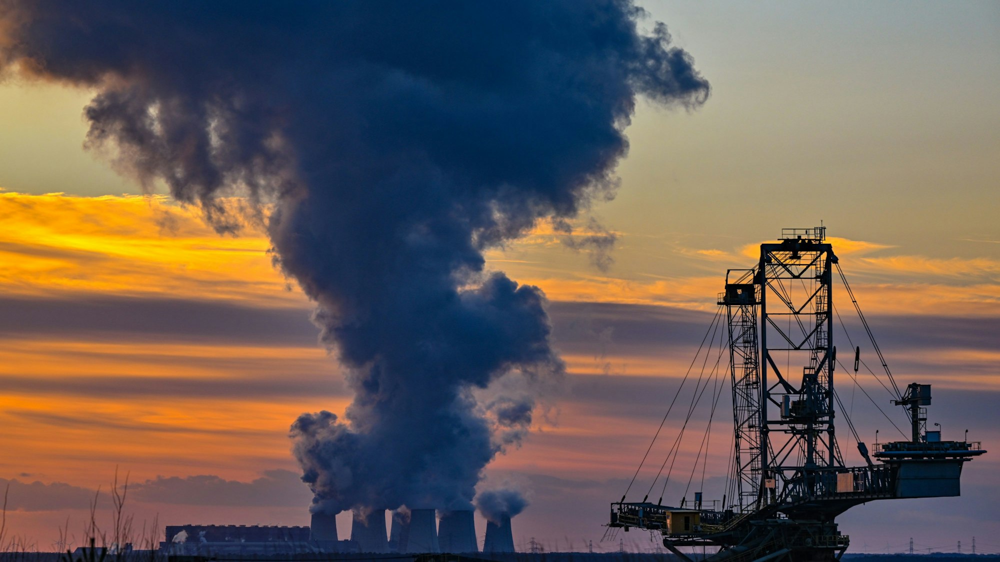 Wasserdampf steigt im Sonnenuntergang am frühen Abend aus den Kühltürmen des Braunkohlekraftwerks Jänschwalde der Lausitz Energie Bergbau AG (LEAG). Im Vordergrund steht ein Absetzer vom Tagebau Jänschwalde.
