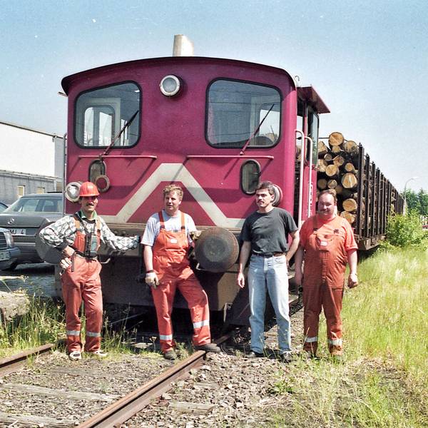 Vier Männer vor einer kleinen Diesellokomotive mit zwei Waggons