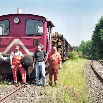 Vier Männer vor einer kleinen Diesellokomotive mit zwei Waggons