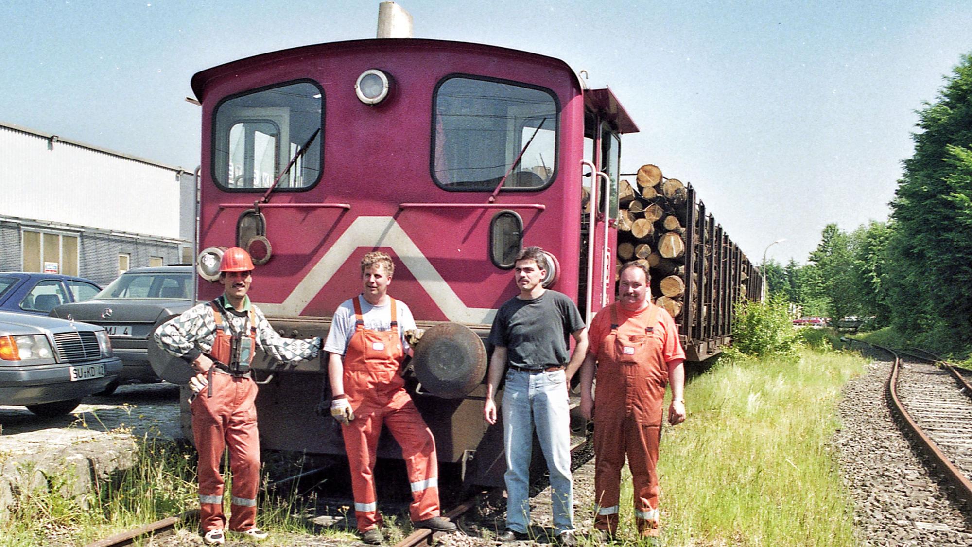 Vier Männer vor einer kleinen Diesellokomotive mit zwei Waggons