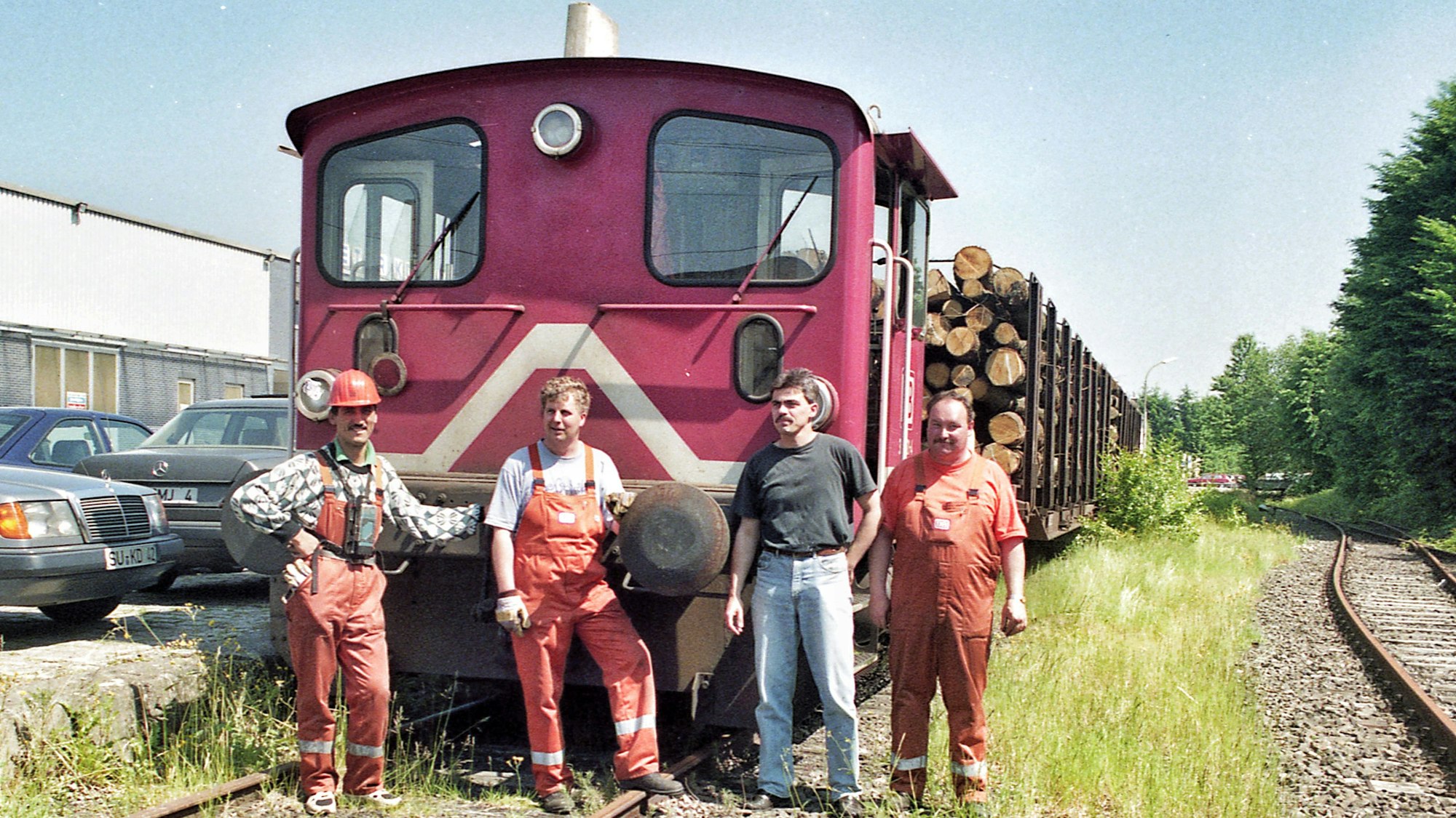Vier Männer vor einer kleinen Diesellokomotive mit zwei Waggons