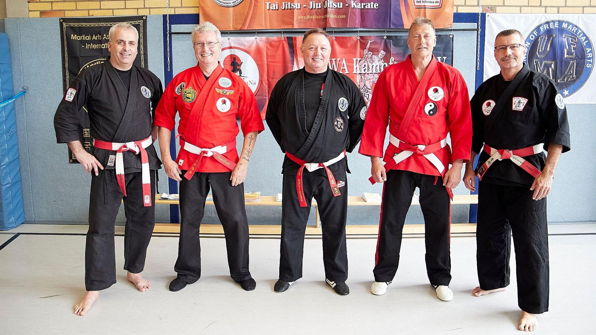 Drei Männer in schwarzen und zwei in schwarz-roten Kampfanzügen stehen in einer Sporthalle. Es sind die Trainer des Budoseminars in Schleiden, zu sehen sind von links Stefan Lang, Paul Taiwa Stanitzek, Rolf Mevißen, Frank Kyselka, Walter Koep.