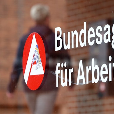 Ein Mann geht an einem Schild mit der Aufschrift „Bundesagentur für Arbeit“ vorbei.
