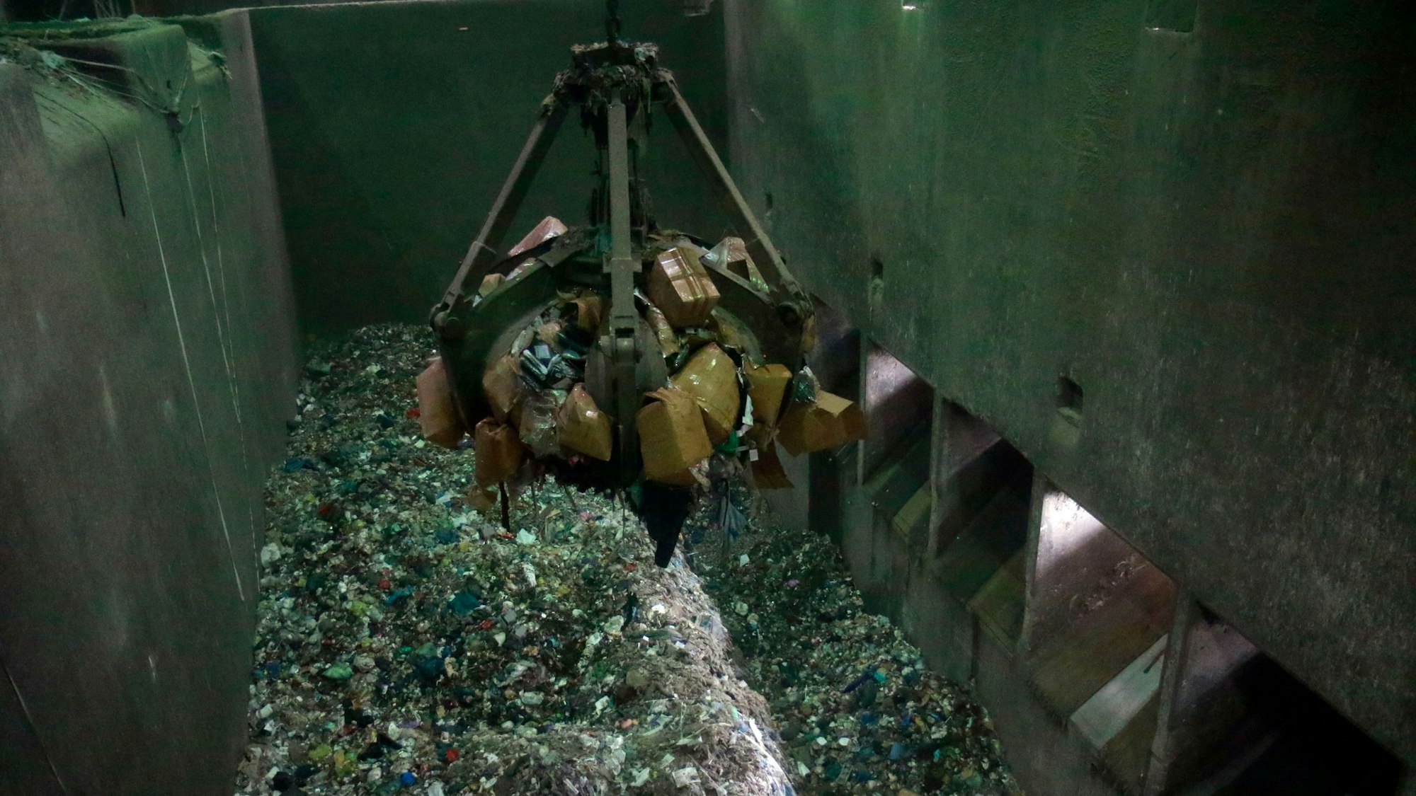 Ein Greifer hebt die Kisten aus der Müllabladehalle in einen Trichter der Brennkammer.