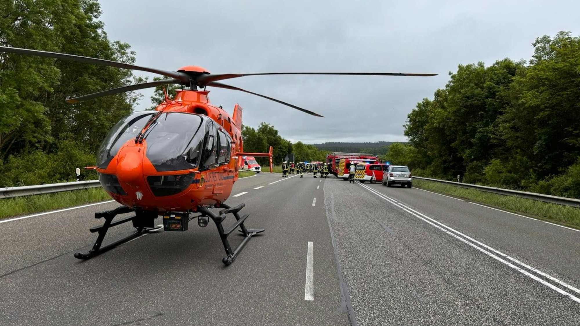 Ein roter Hubschrauber steht auf der B51, im Hintergrund sind Rettungswagen sowie Einsatzfahrzeuge der Feuerwehr zu erkennen.