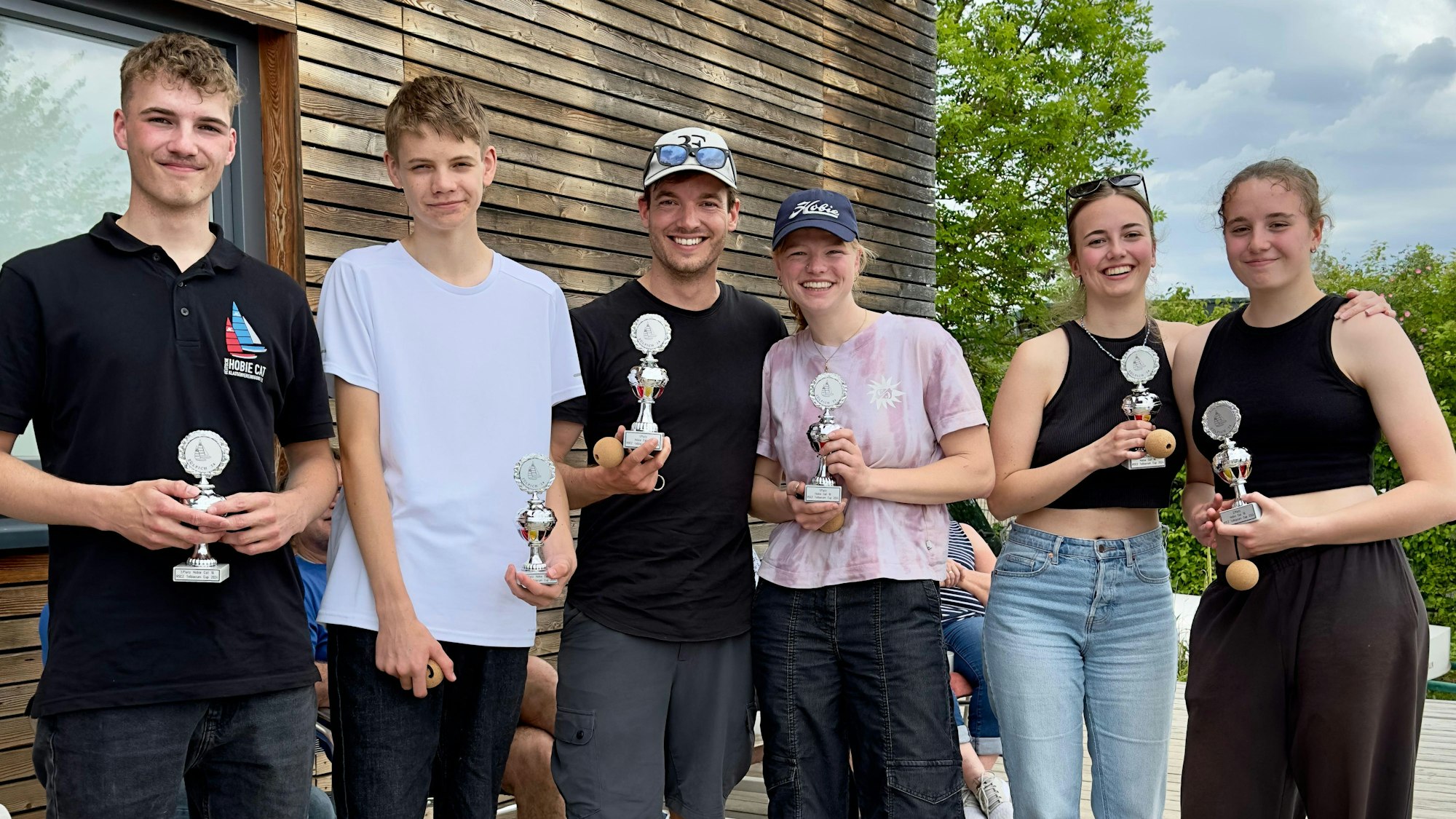 Segler halten nach dem Turnier ihre Pokale in die Kamera.