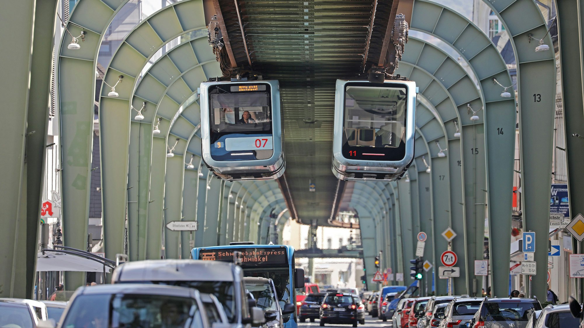 Die Schwebebahnen von Wuppertal fahren durch den Stadtteil Vohwinkel.
Darunter sind Autos im Straßenverkehr zu sehen.