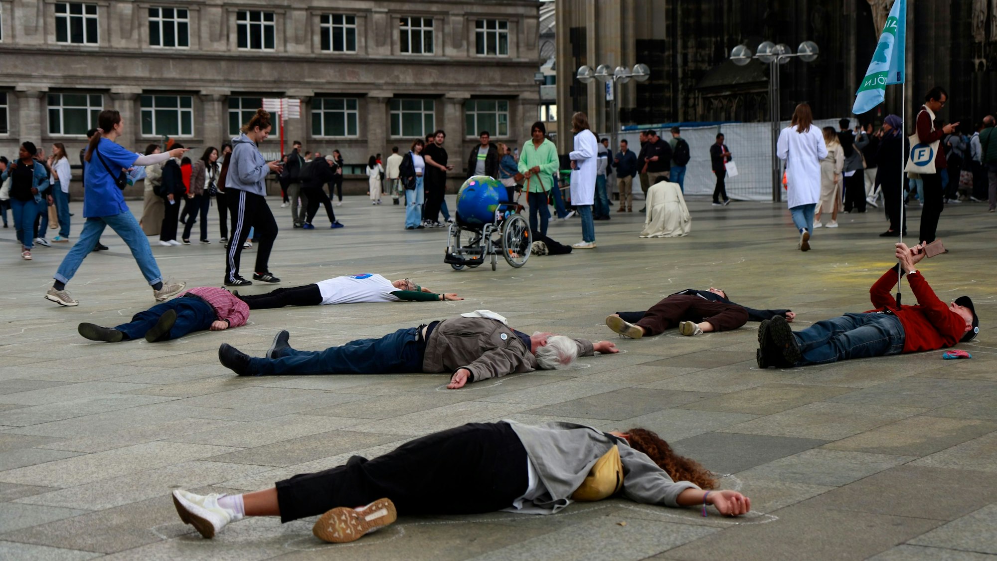 Menschen liegen vor dem Kölner Dom reglos auf dem Boden.