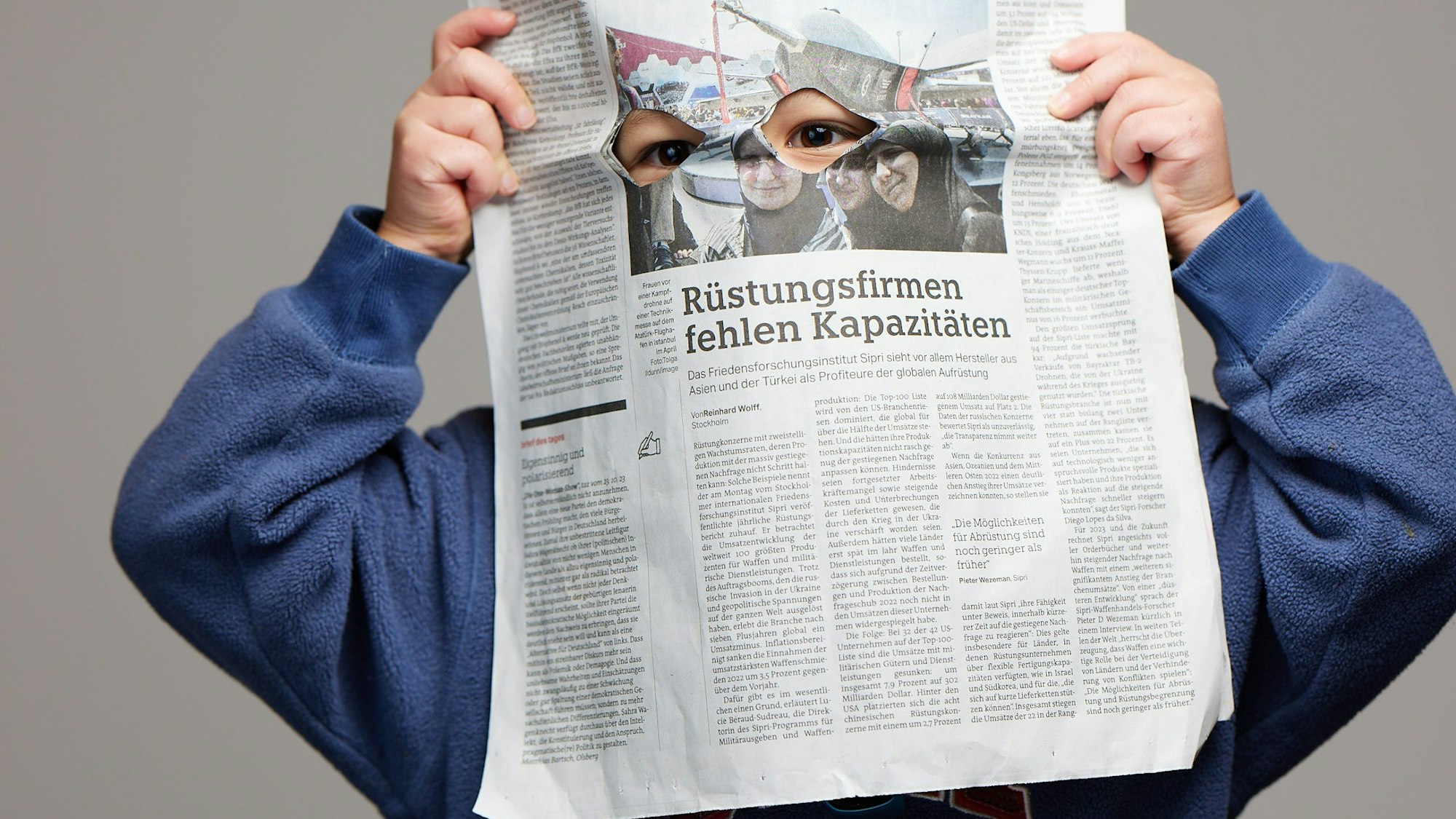 Ein Kind versteckt sich hinter einer Zeitungsseite, die Augen lugen durch in die Zeitung geschnittene Löcher.