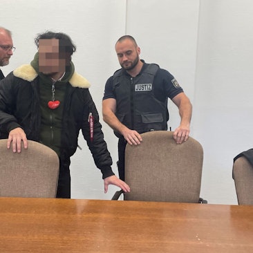 Der Angeklagte mit seinem Verteidiger Jörg Hardies und einem Wachtmeister beim Prozessauftakt im Kölner Landgericht