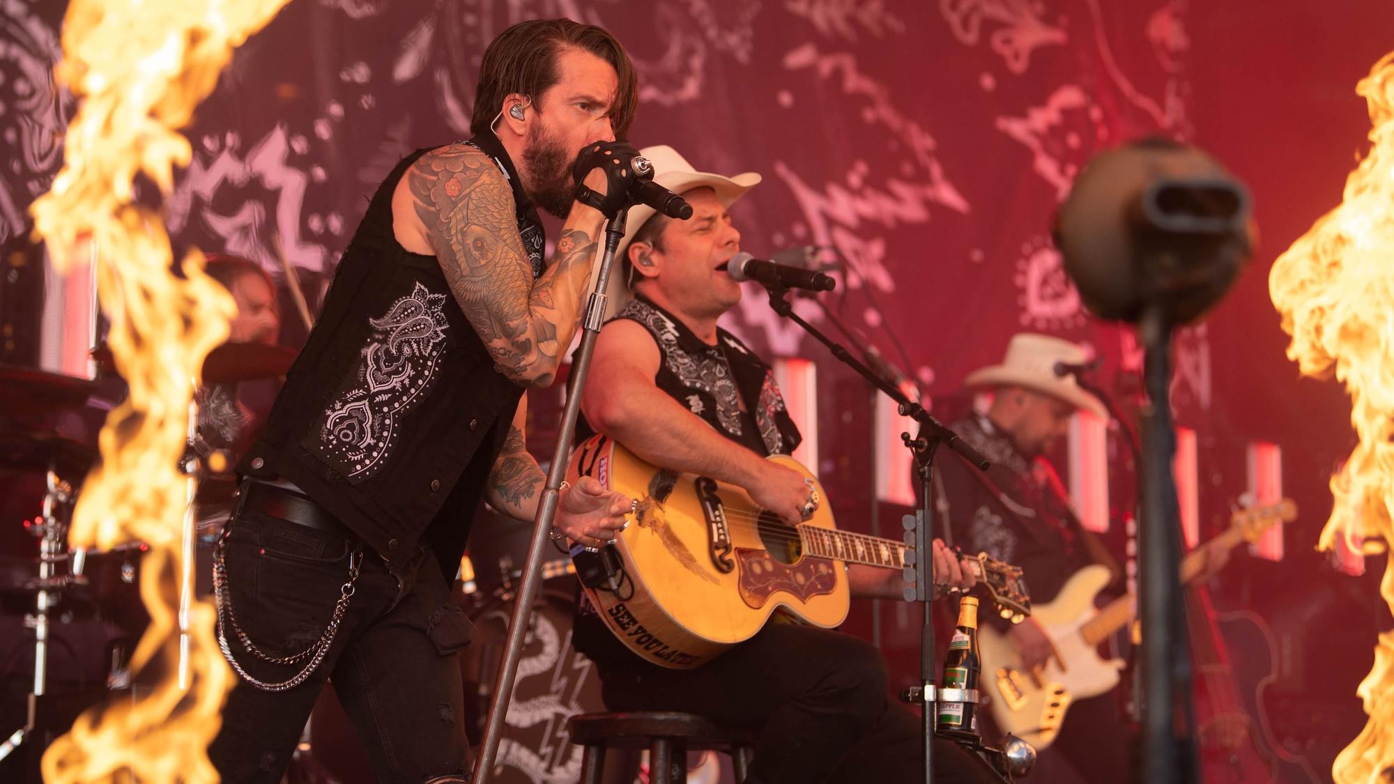 Die Band Bosshoss spielt bei einem Konzert, am Bildrand sind Flammen zu sehen.