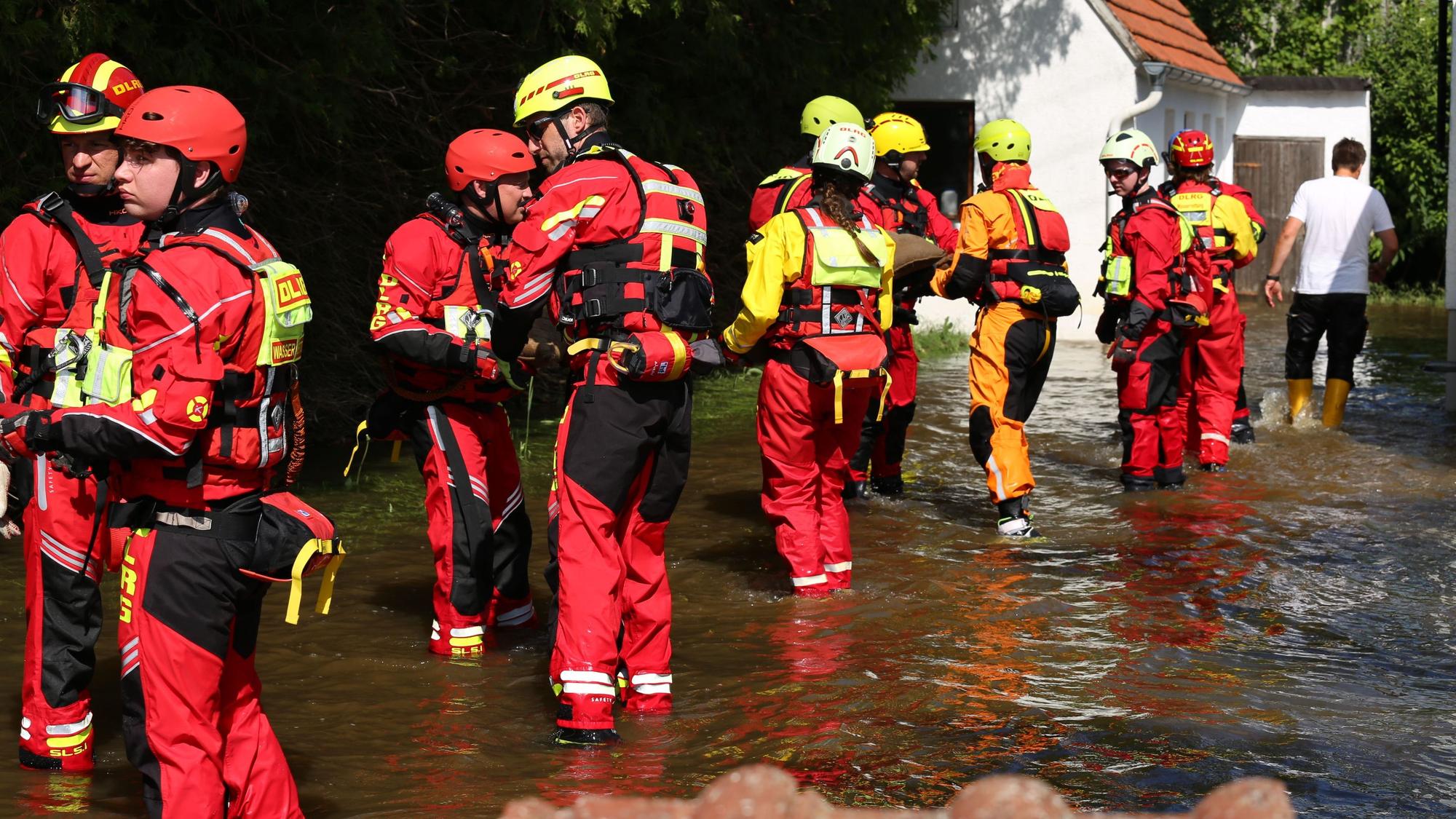 DLRG-Retter reichen in einer Menschenkette Sandsäcke weiter durchs knöchelhohe Wasser auf einer überfluteten Straße.