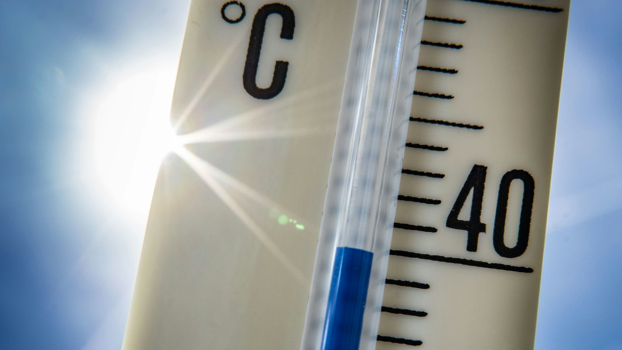 Ein Außenthermometer zeigt vor dem blauen Himmel und der Sonne eine Temperatur von nahezu 40 Grad Celsius an.