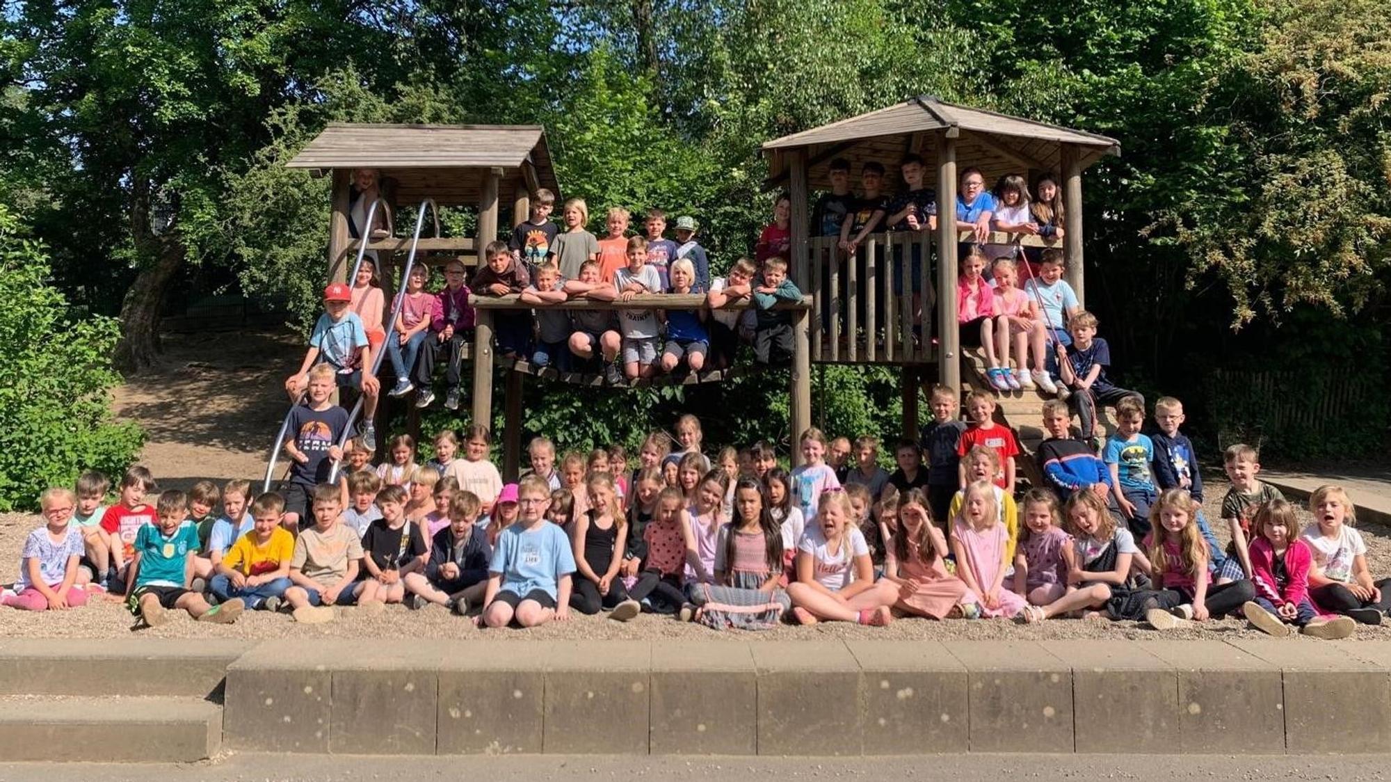 Die Kinder der Grundschule in Süng haben sich zum Gruppenbild auf dem Spielplatz aufgestellt. Rund 150 Kinder sitzen auf den Klettertürmen, im Sandkasten und weiteren Spielgeräten.
