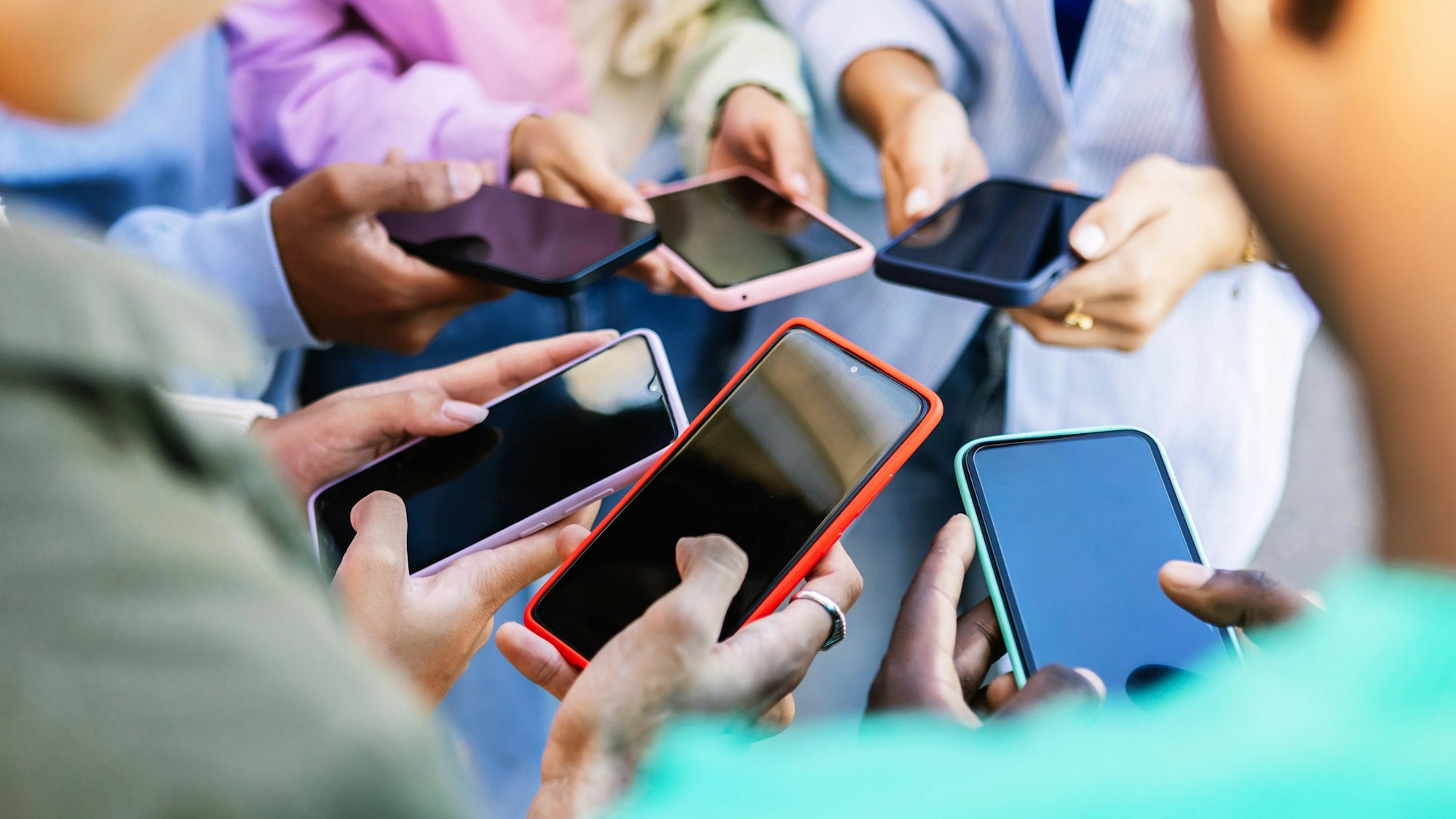Eine Gruppe Jugendlicher steht mit gezückten Handys im Kreis.