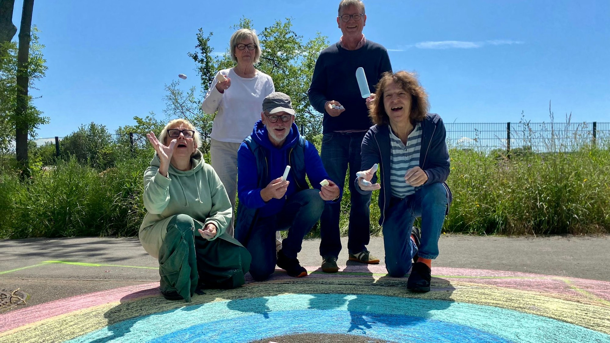 Anne Bergmann (v.l.), Beate Thorstensen, Leo Schmidt, Uli Norgall-Hambach und Thomas Latzke posieren über einem Regenbogen aus Straßenkreide und werfen die Kreide in die Luft.
