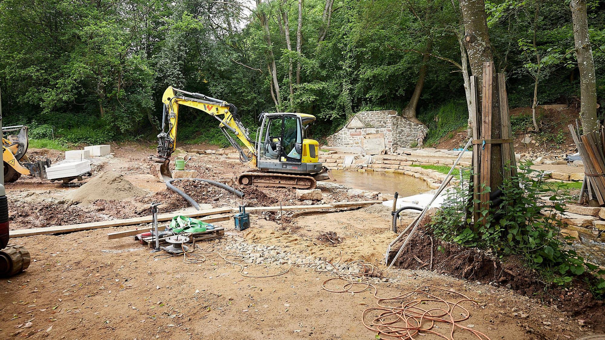 Ein gelber Bagger steht auf einer Baustelle im Wald: Hier wird bei Nettersheim-Holzmülheim der Park an der Erftquelle umgebaut.