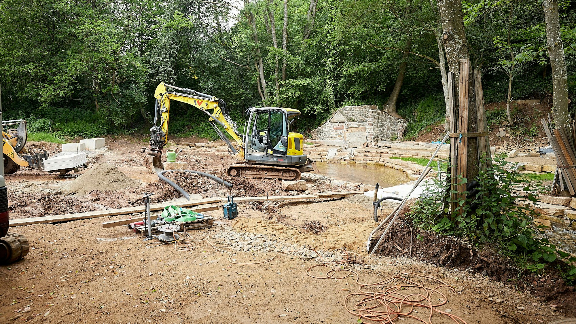 Ein gelber Bagger steht auf einer Baustelle im Wald: Hier wird bei Nettersheim-Holzmülheim der Park an der Erftquelle umgebaut.
