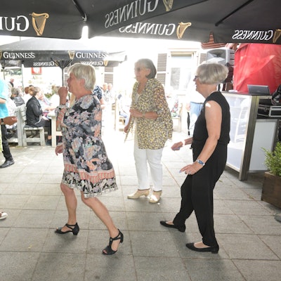 Tanzende Frauen und ein Pärchen unter einem Sonnenschirm.