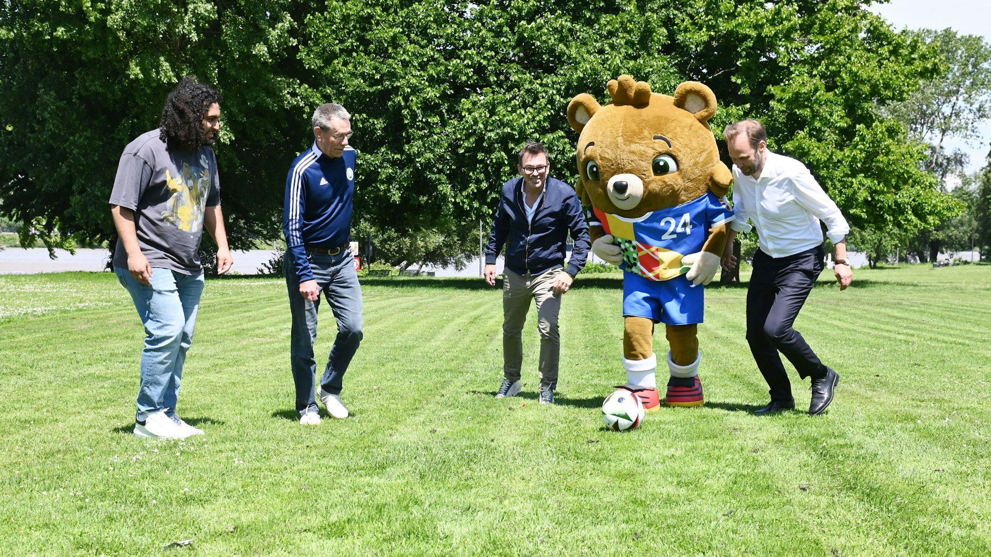 Vier Männer spielen mit einem Maskotten Fußball