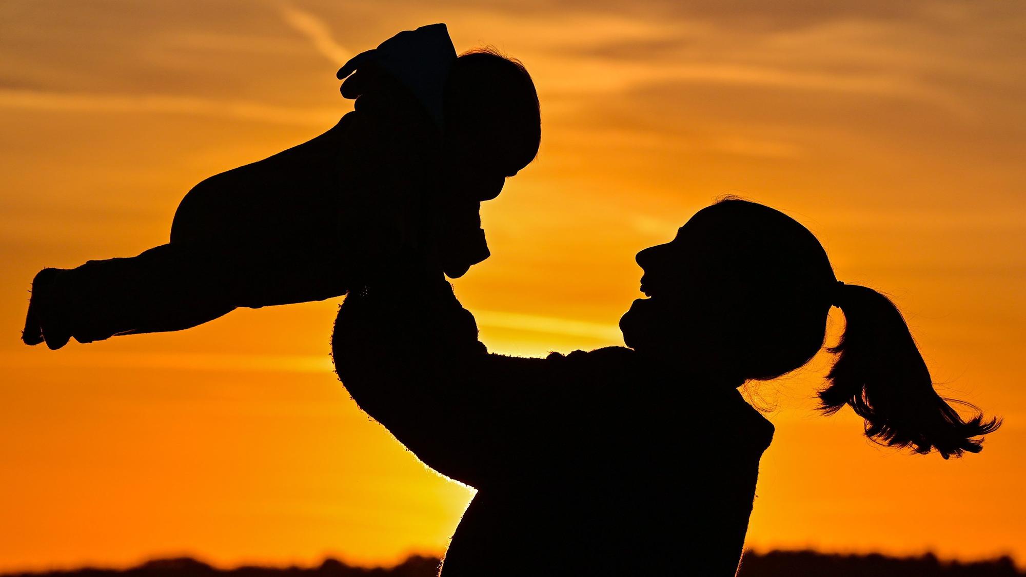 Eine Mutter ist mit ihrem acht Monate alten Baby im Sonnenuntergang auf einem Feldweg zu sehen.
