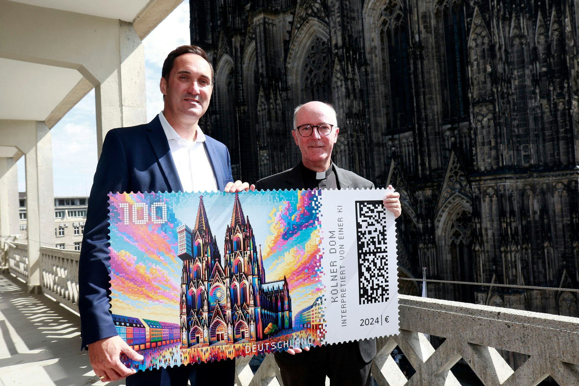 Dompropst Guido Assmann (rechts) und Alexander Plum, Deutsche Post, bei der Vorstellung der KI-generierten Briefmarke mit dem Kölner Dom.