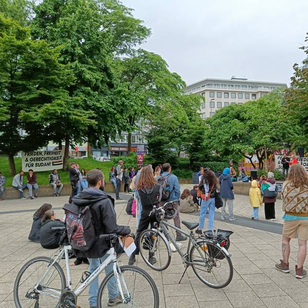 Menschen stehen um eine Erhöhung am Ebertplatz und hören eine Rede.
