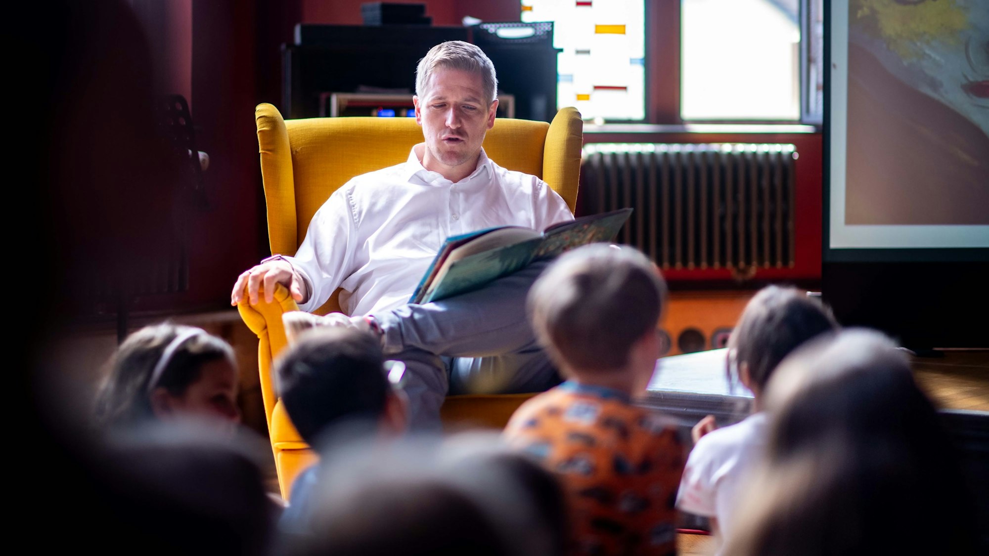 Das Bild zeigt Landrat Markus Ramers. Er sitzt in einem gelben Sessel. Auf seinem Bein liegt ein Buch.