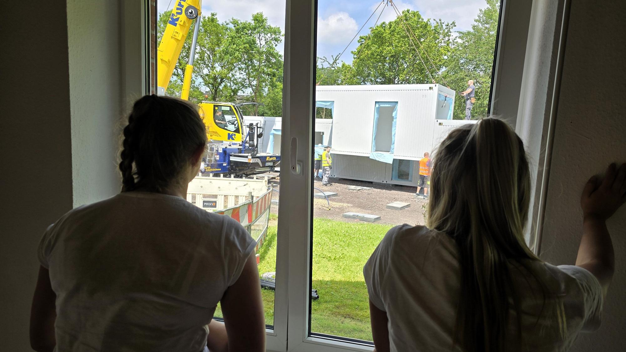 Zwei Frauen schauen aus einem Fenster und beobachten, wie Container abgeladen werden.