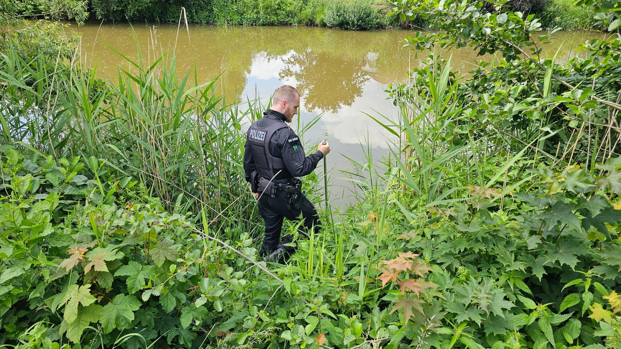 Ein Polizist sucht an einem Gewässer in Döbeln nach einem neunjährigen Mädchen, das als vermisst gemeldet wurde.