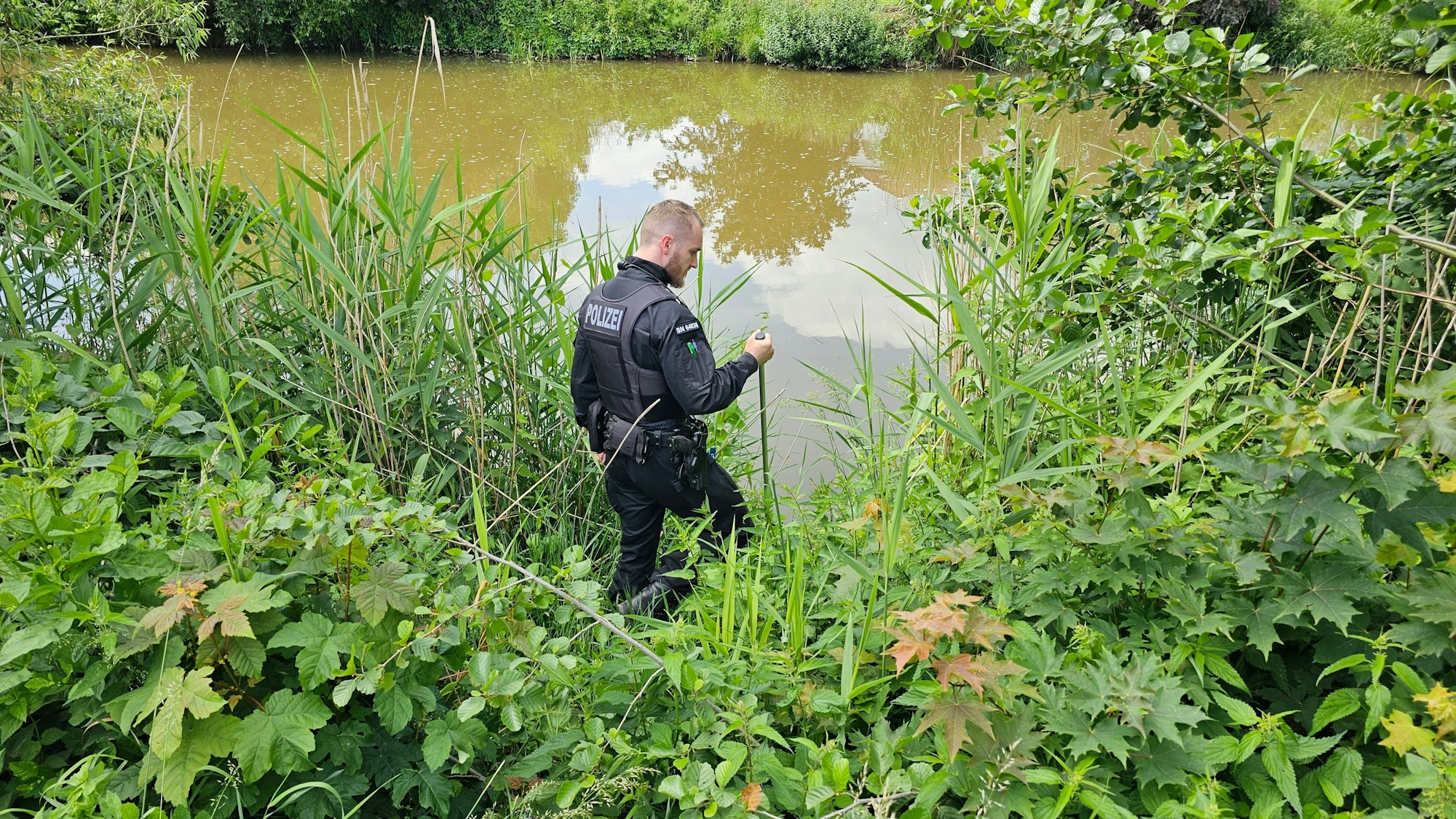 Ein Polizist sucht an einem Gewässer in Döbeln nach einem neunjährigen Mädchen, das als vermisst gemeldet wurde.