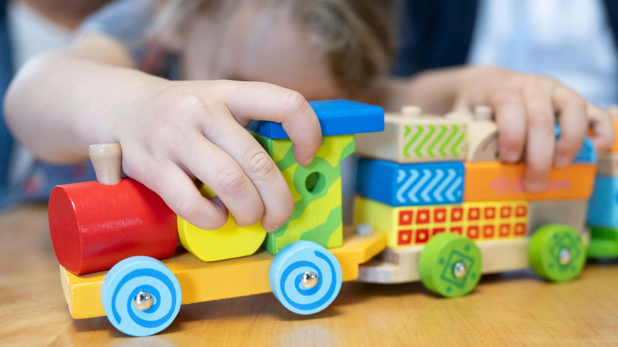 Ein Kind spielt mit einer bunten Holzeisenbahn.