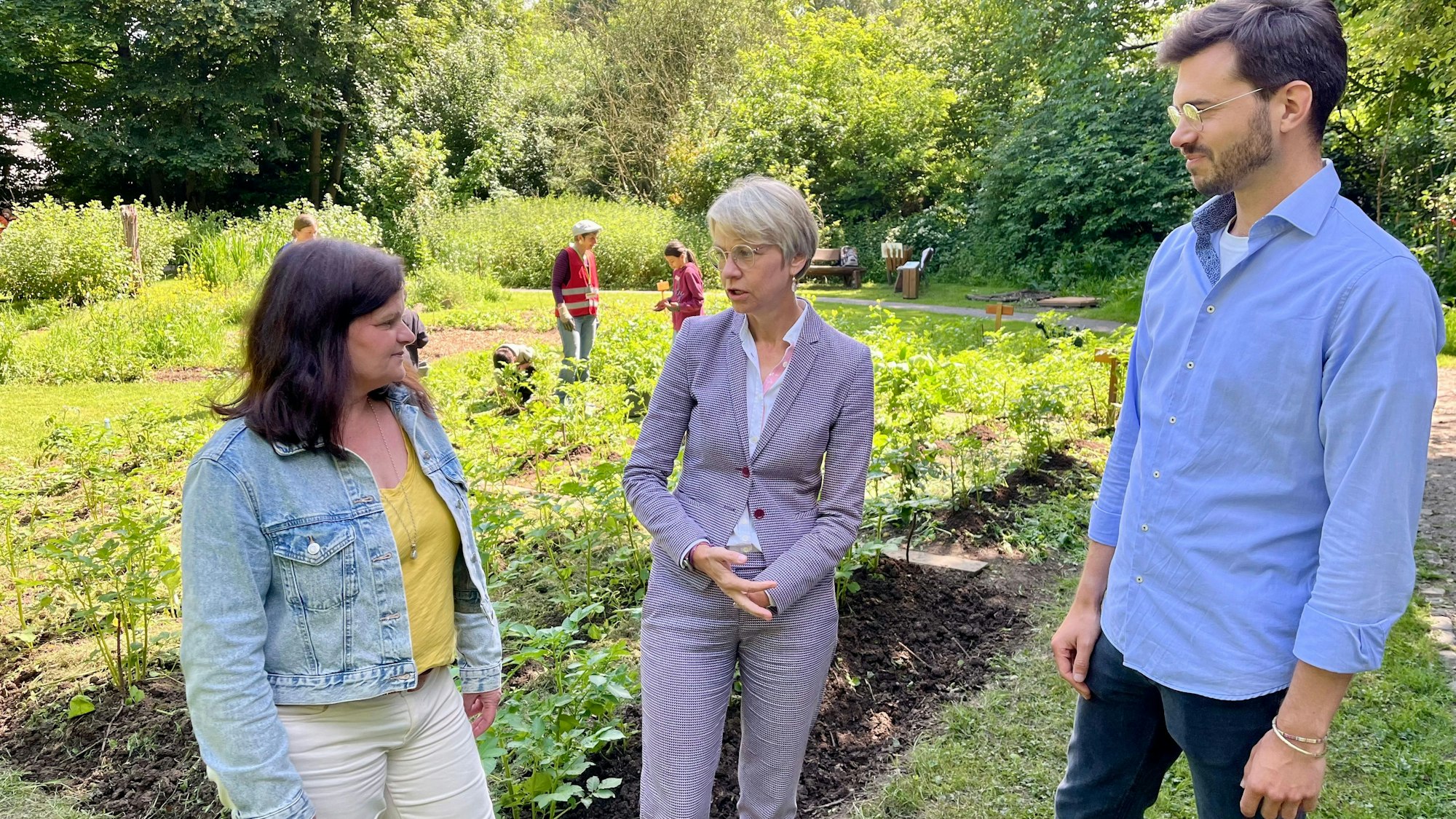 Schulministerin Feller (M.) lässt sich von Marianne Ackermann und Lars Dietrich das Naturgut Ophoven – hier den Schulgarten – zeigen.