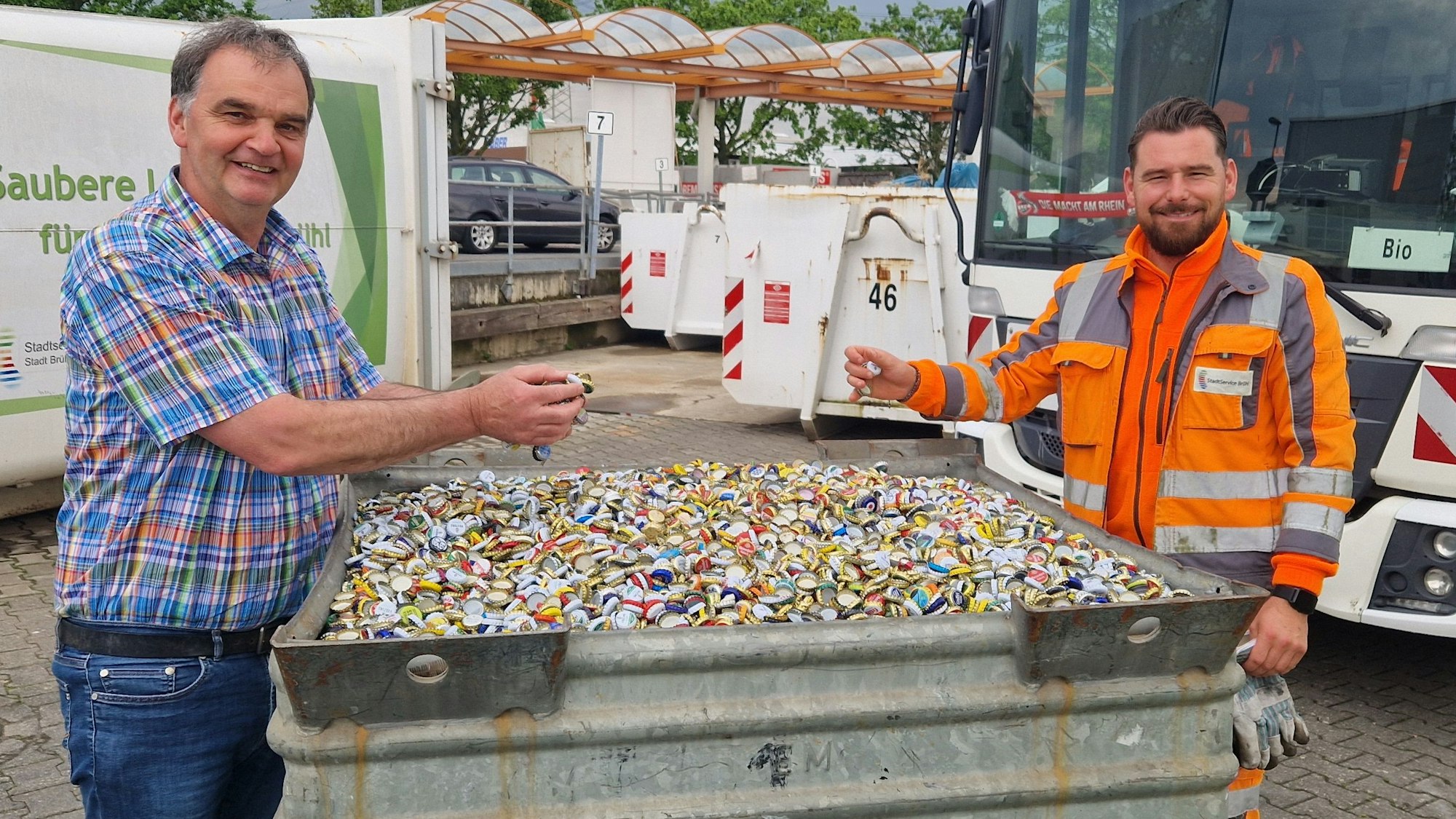 Zu sehen sind zwei Mitarbeiter vom Stadtservice, die an einem mit Kronkorken gefüllten Behältnis stehen.