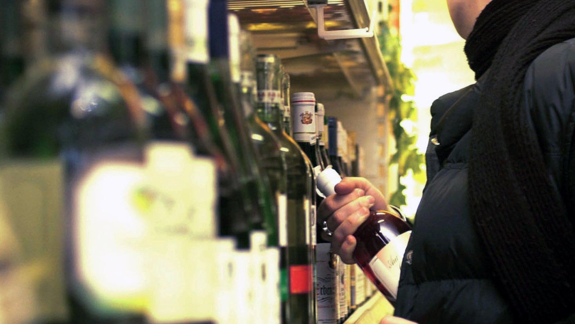 Das Bild zeigt eine Person in einem Wein-Regal, der eine Flasche in die Jacke steckt.