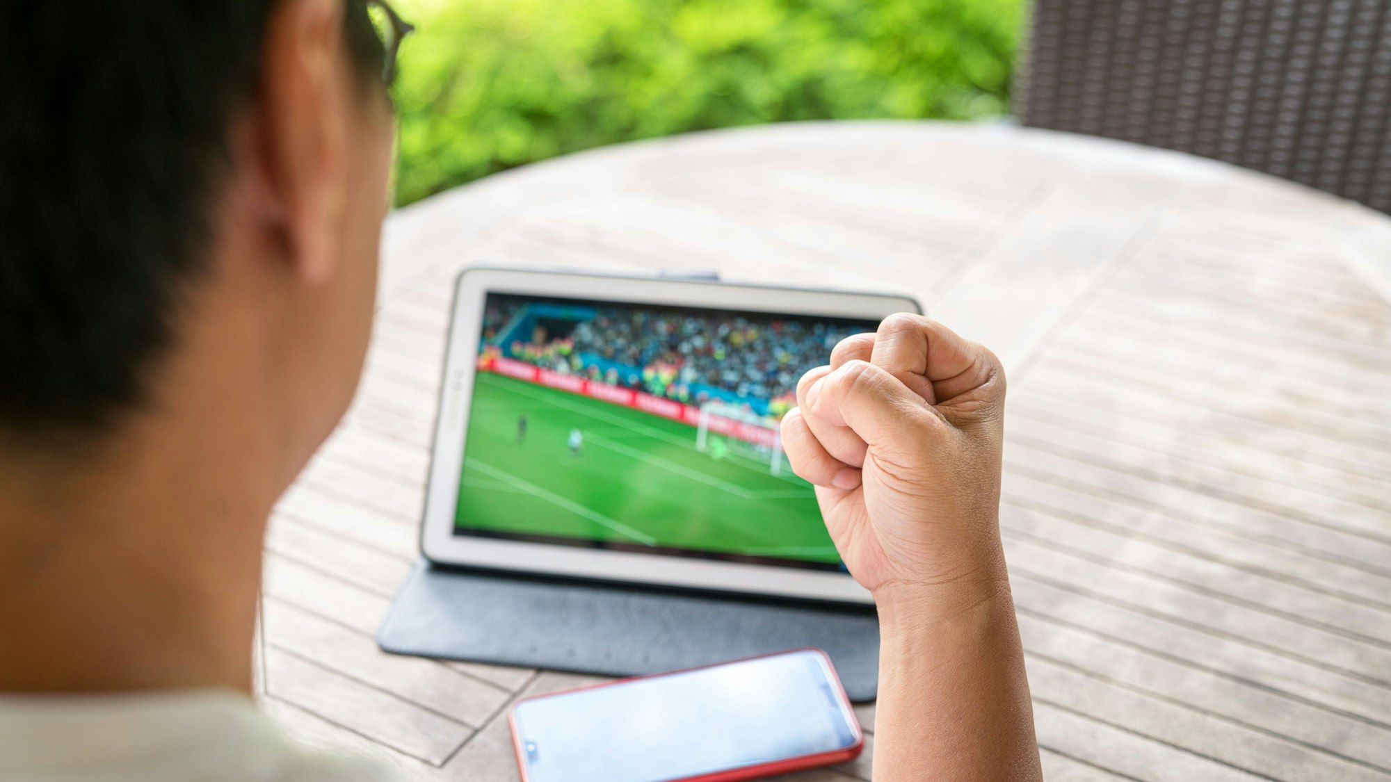 Ein Mann schaut im Garten ein Fußballspiel auf seinem Tablet