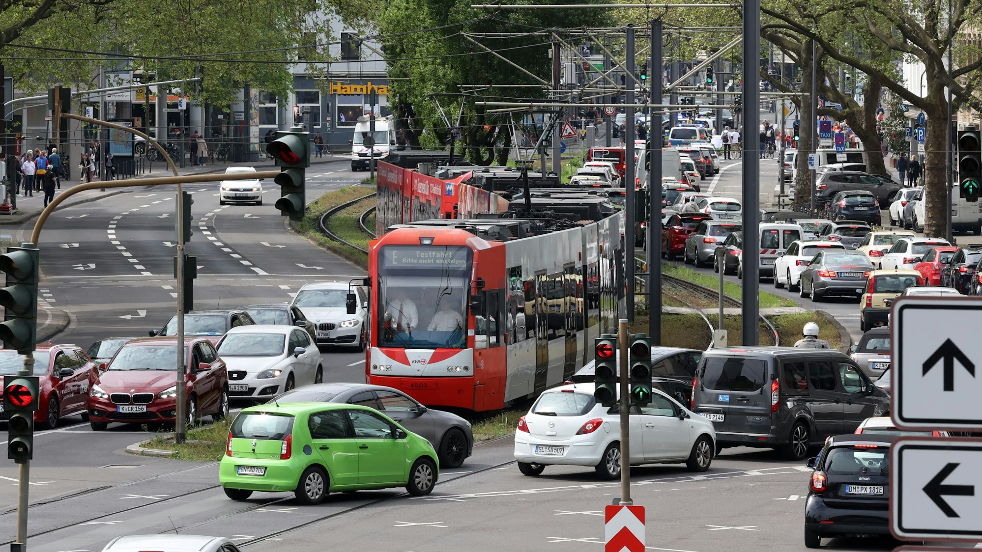 Eine Straßenbahn hält auf der Cäcilienstraße an einer Ampel, während vor ihr Fahrzeuge die Kreuzung zum Neumarkt passieren. Die Straßenbahn verfügt hier über kein eigenes Gleisbett.