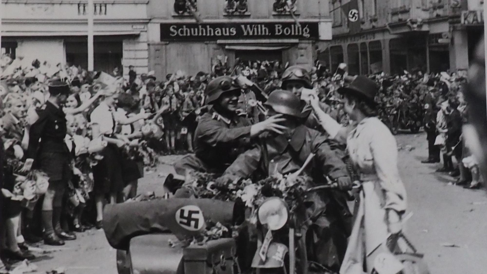 Soldaten auf einem Motorrad mit Beiwagen fahren auf den Euskirchener Marktplatz. Am Rand stehen jubelnde Menschen.