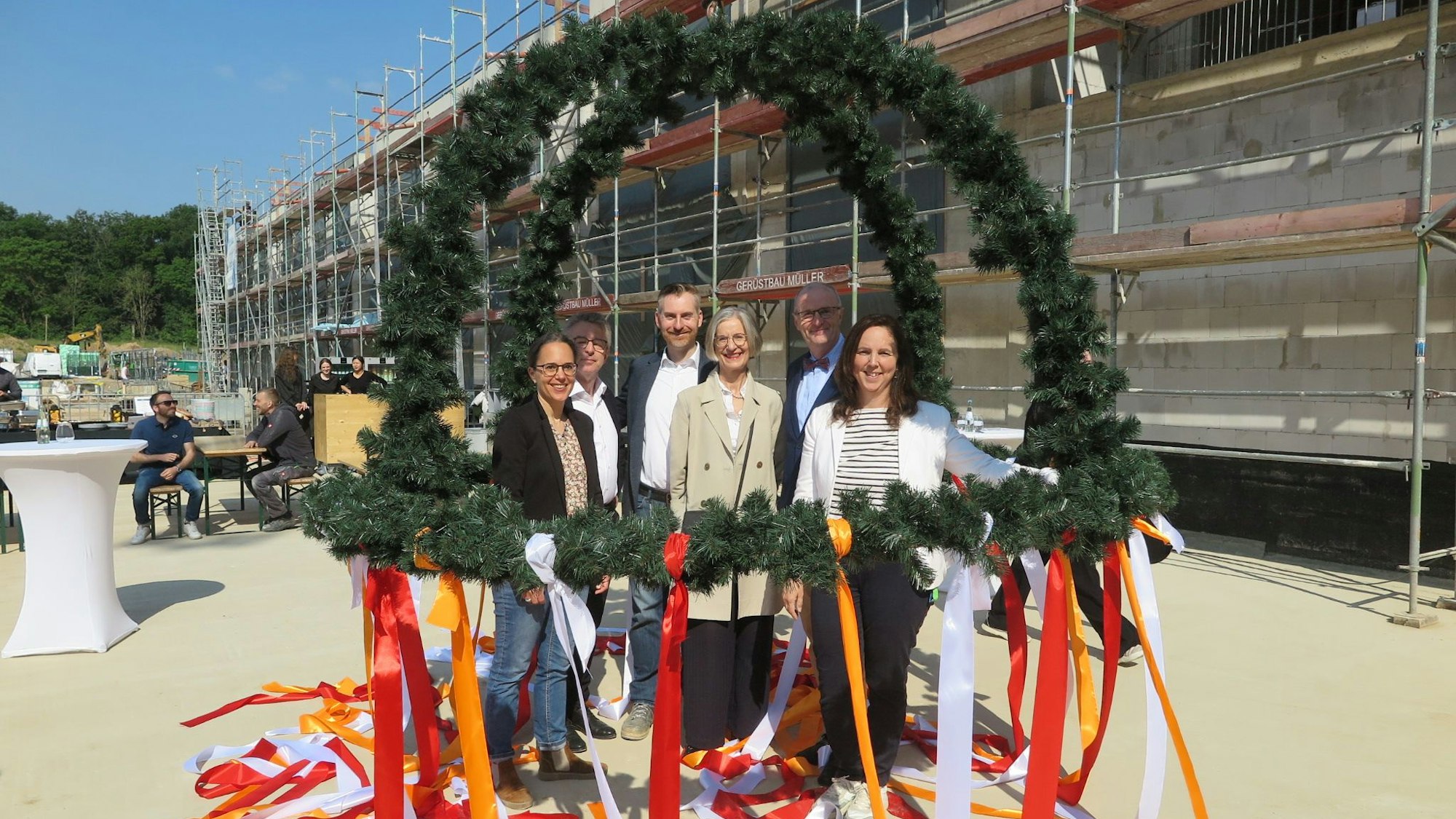 Menschen mit einem Richtfestkranz vor einem Rohbau