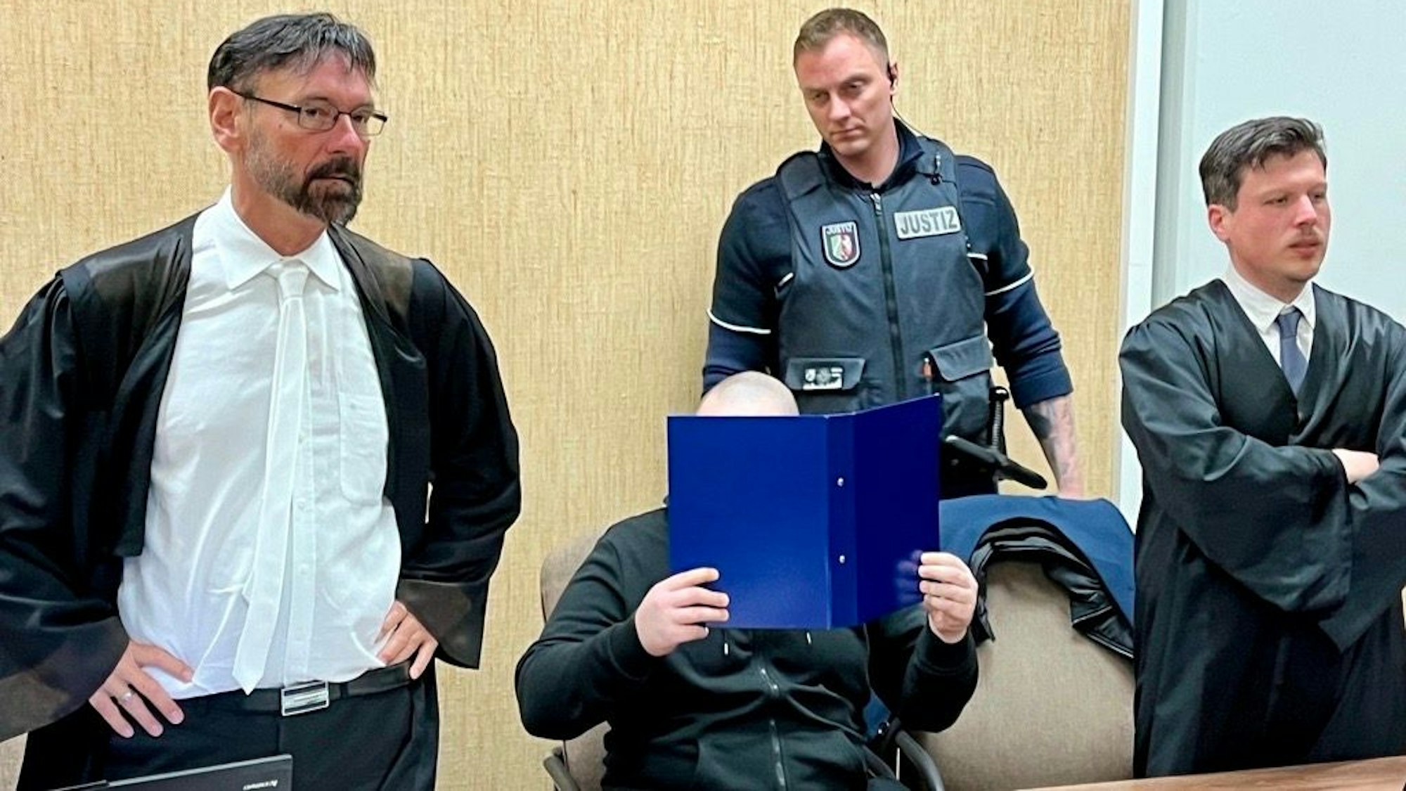 Der Beschuldigte mit seinen Verteidigern und einem Wachtmeister beim Prozessauftakt im Kölner Landgericht