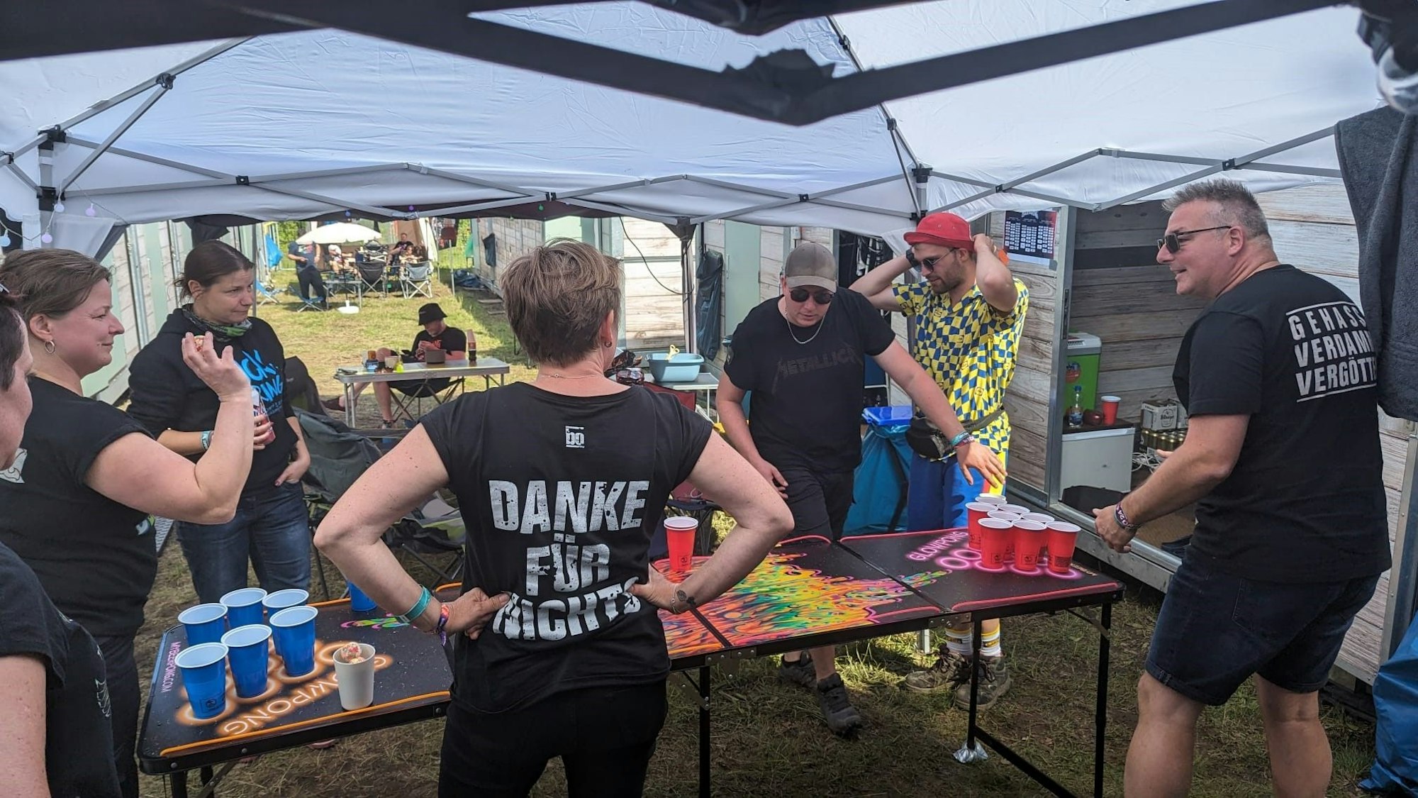 Eine Gruppe von Menschen steht an einem Beer-Pong-Tisch unter einem Pavillon auf einem Camping-Platz.