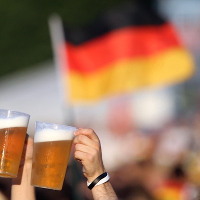 Zwei Bierbecher werden von Fußball-Fans vor einer Deutschland-Fahne in die Höhe gehalten. (Symbolbild)