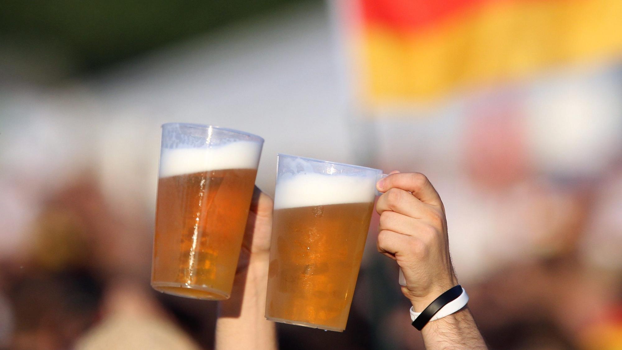 Zwei Bierbecher werden von Fußball-Fans vor einer Deutschland-Fahne in die Höhe gehalten. (Symbolbild)