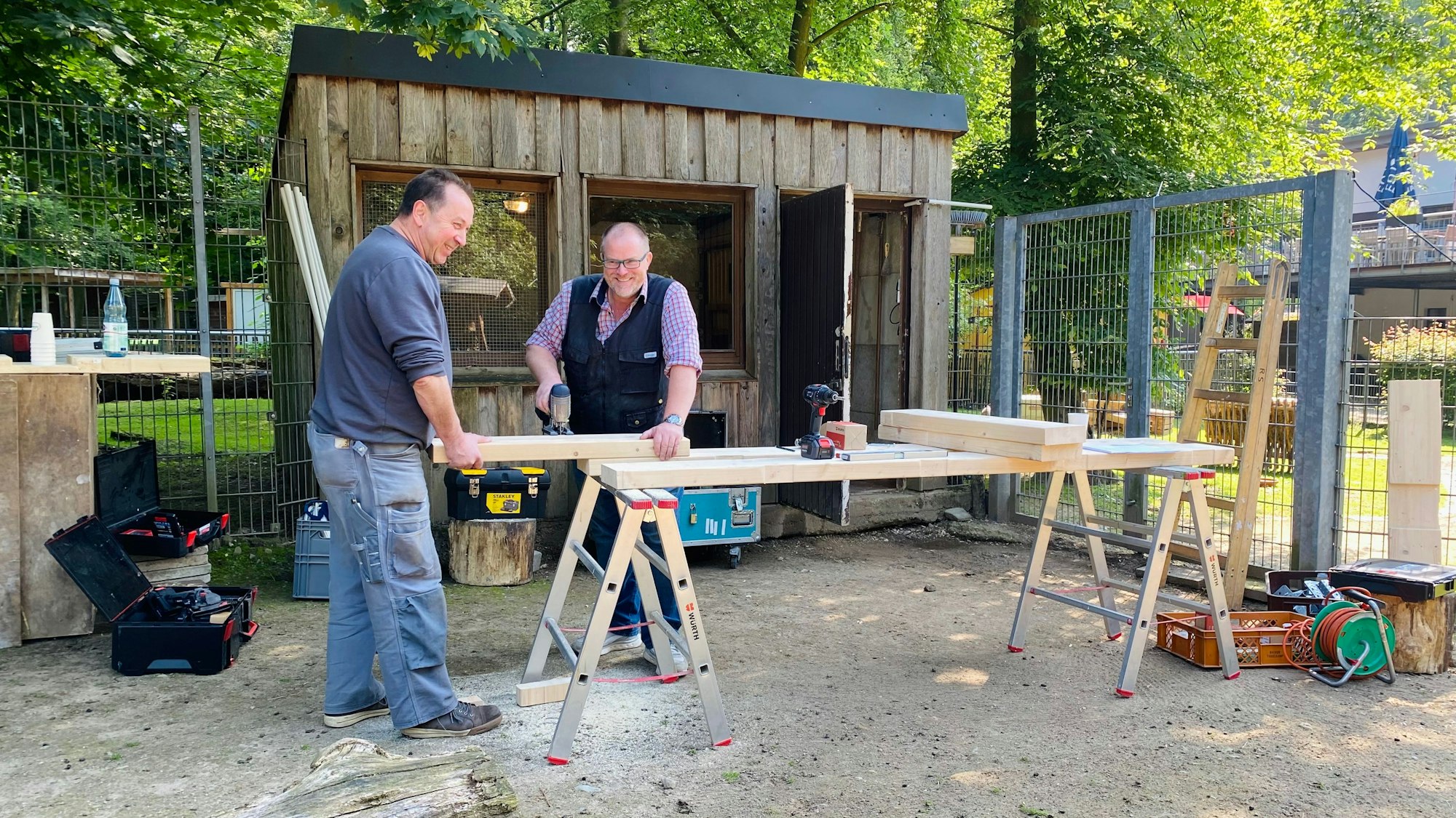 Zwei Männer sägen Holz vor einem Stall.