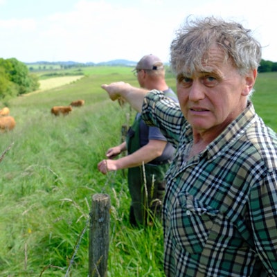 Der Landwirt Paul Milz deutet mit ausgestrecktem Arm auf die Weide, wo einige seiner Rinder stehen. Sein Kollege Marcel May steht neben ihm.